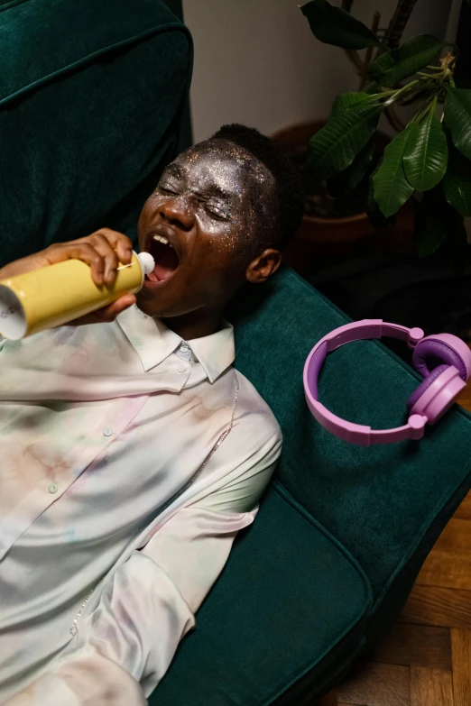 a man laying on a couch with a banana in his mouth, an album cover, trending on pexels, hyperrealism, rainbow colored dust mask, adut akech, drinking champagne, purple liquid