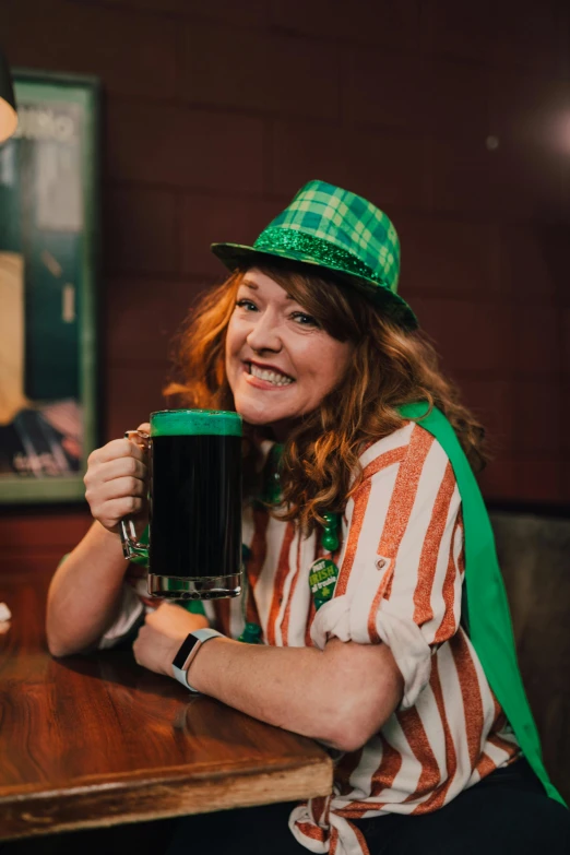 a woman sitting at a table with a mug of beer, wearing green tophat, striped, celtic culture, 2019 trending photo