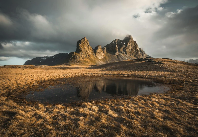 a body of water sitting on top of a grass covered field, by Sebastian Spreng, unsplash contest winner, land art, craggy mountains, mordor, medium format, brown