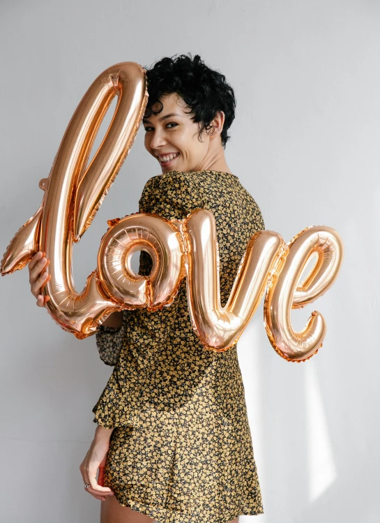 a woman holding a balloon shaped like the word love, by Julia Pishtar, metallic, thumbnail, patterned clothing, official product photo