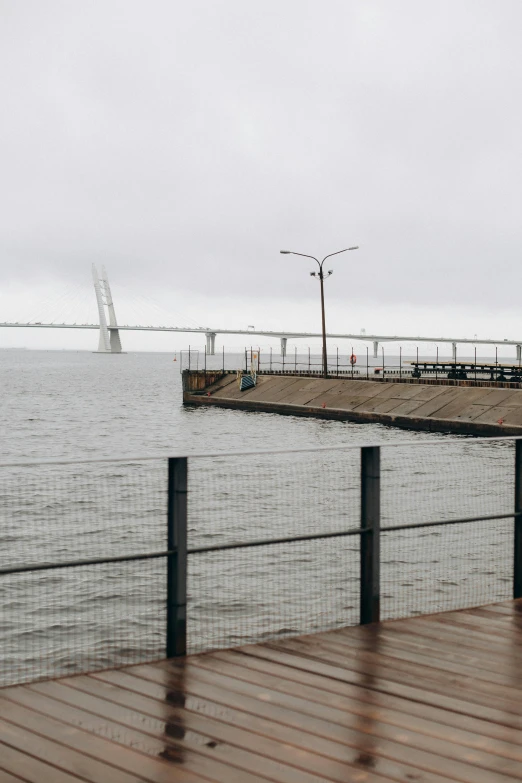 a pier next to a body of water with a bridge in the background, by Daarken, overcast gray skies, in savannah, wall of water either side, port city