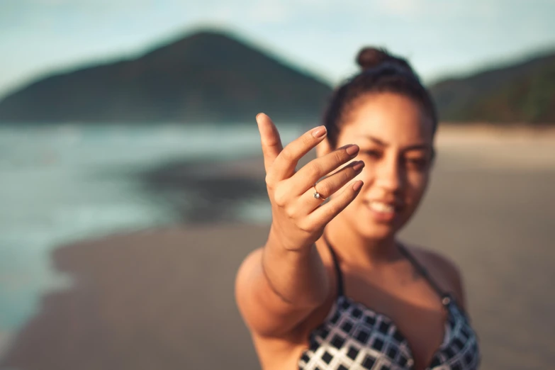a woman standing on top of a sandy beach, pexels contest winner, happening, point finger with ring on it, mixed-race woman, photoshoot for skincare brand, shallow depth of focus