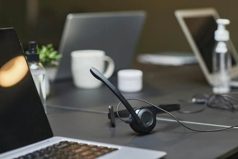 a laptop computer sitting on top of a wooden table, wearing a headset, black wired cables, coworkers, detailed product image