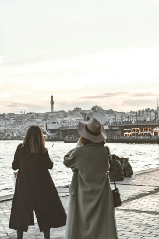 a couple of women standing next to a body of water, pexels contest winner, modernism, harbour, walking away from camera, fallout style istanbul, cornwall