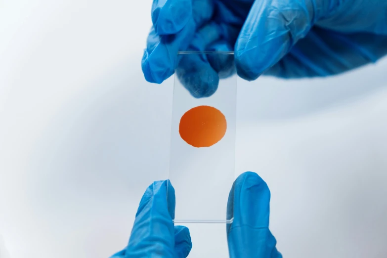 a person in blue gloves holding a piece of paper, a microscopic photo, orange color, transparent liquid, high quality product image”, highly capsuled