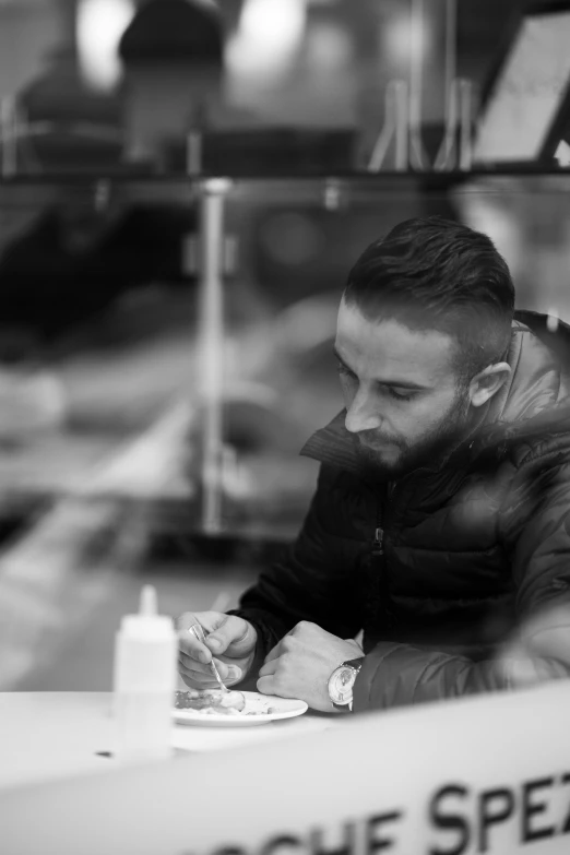 a man sitting at a table writing on a piece of paper, a black and white photo, inspired by Ahmed Yacoubi, snacks, profile pic, low quality photo, stefano brunesci