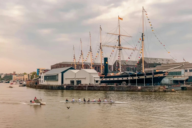 a group of people rowing on top of a body of water, happening, hull, building along a river, profile image, sailing ships