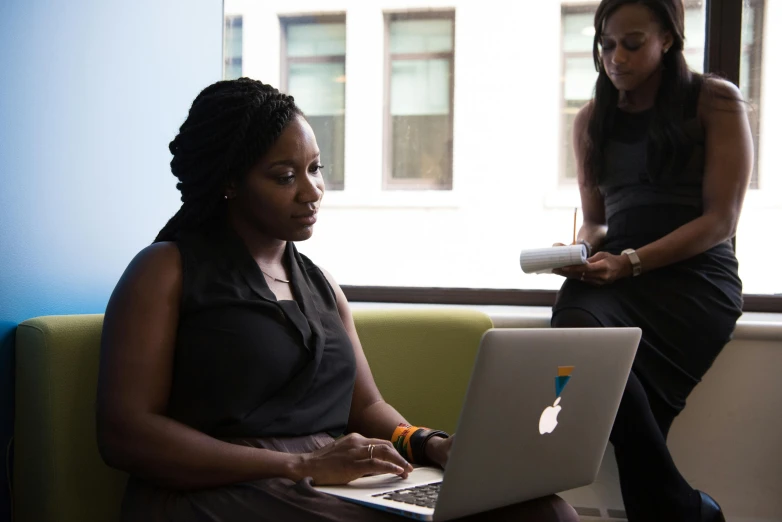 a woman sitting on a couch using a laptop computer, by Arabella Rankin, pexels contest winner, two women, ( ( dark skin ) ), sat in an office, standing still