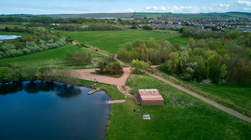 a large body of water sitting next to a lush green field, by John Henderson, land art, adventure playground, fpv, dunwall city, in a park and next to a lake