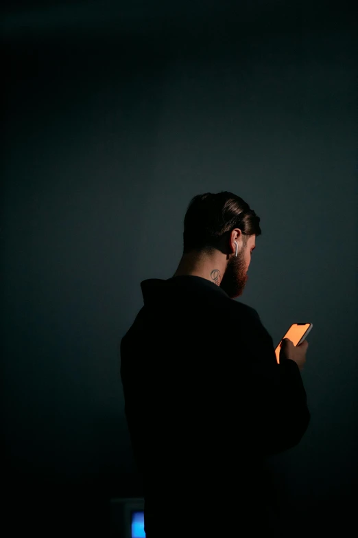 a man looking at his cell phone in the dark, pexels, minimalism, with a beard and a black shirt, trying to read, back - lit, felix englund