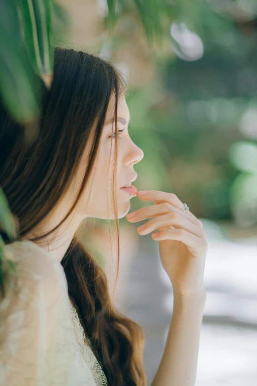 a woman in a white dress standing next to a tree, inspired by Elsa Bleda, trending on pexels, renaissance, hand on her chin, young woman with long dark hair, sideview, soft green natural light