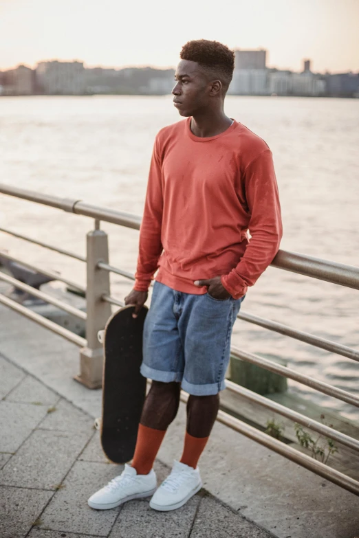 a young man standing by the water holding a skateboard, by Eglon van der Neer, trending on unsplash, renaissance, long orange sweatshirt, wearing red shorts, brooklyn, thumbnail