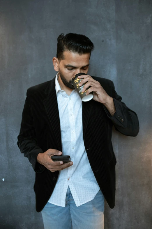 a man drinking from a cup while standing next to a wall, trending on pexels, looking at his phone, wearing causal black suits, portrait of danny gonzalez, promotional image