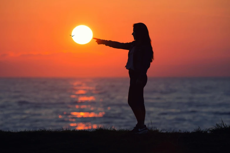 a woman standing on top of a grass covered field next to the ocean, pexels contest winner, with two suns in the sky, silhouette :7, holding a ray gun, profile pic