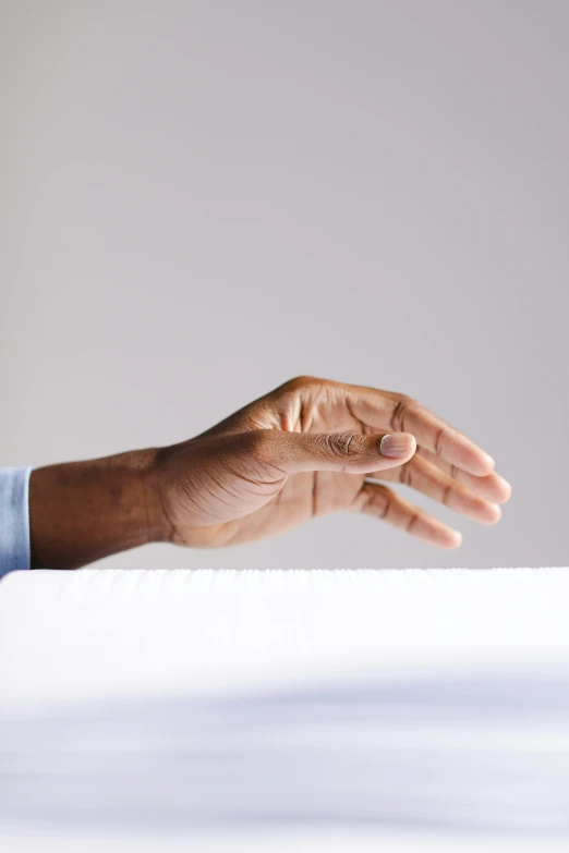 a close up of a person's hand holding a piece of paper, by James Morris, unsplash, hyperrealism, on a white table, shrugging, backlighted, raised hand