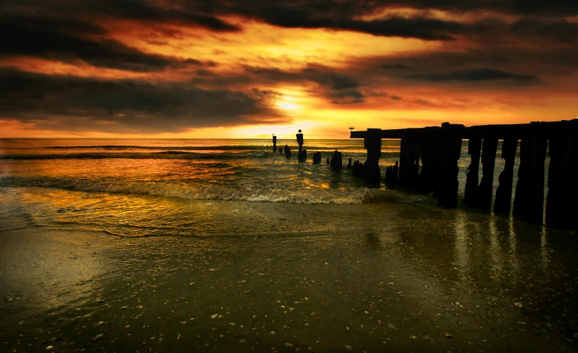 a couple of people standing on top of a beach next to the ocean, inspired by Andreas Achenbach, pexels contest winner, pillars, golden hues, omaha beach, apocalyptic setting