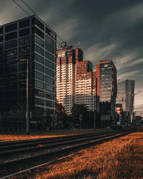 a train traveling down train tracks next to tall buildings, by Adam Marczyński, ominous photo, grass field surrounding the city, golden hour photo, on a dark background