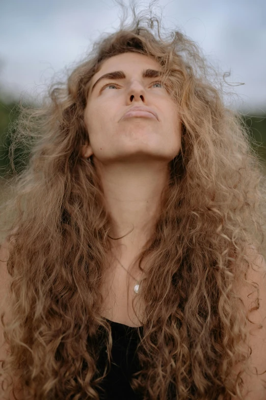 a woman with long curly hair looking up, by Carey Morris, trending on pexels, a still of an ethereal, strong chin, looking to the sky, head tilted down