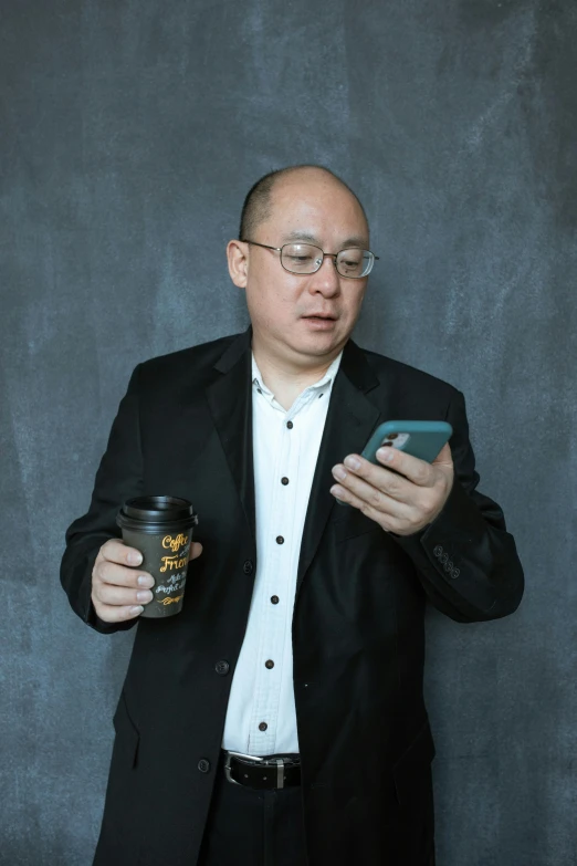 a man holding a cup of coffee and a cell phone, an album cover, inspired by Zhang Kechun, pexels contest winner, neo-dada, standing with a black background, middle aged man, balding, typical cryptocurrency nerd