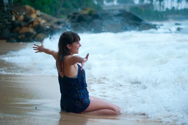 a woman sitting on top of a beach next to the ocean, splashing water, avatar image, sri lanka, waving hands
