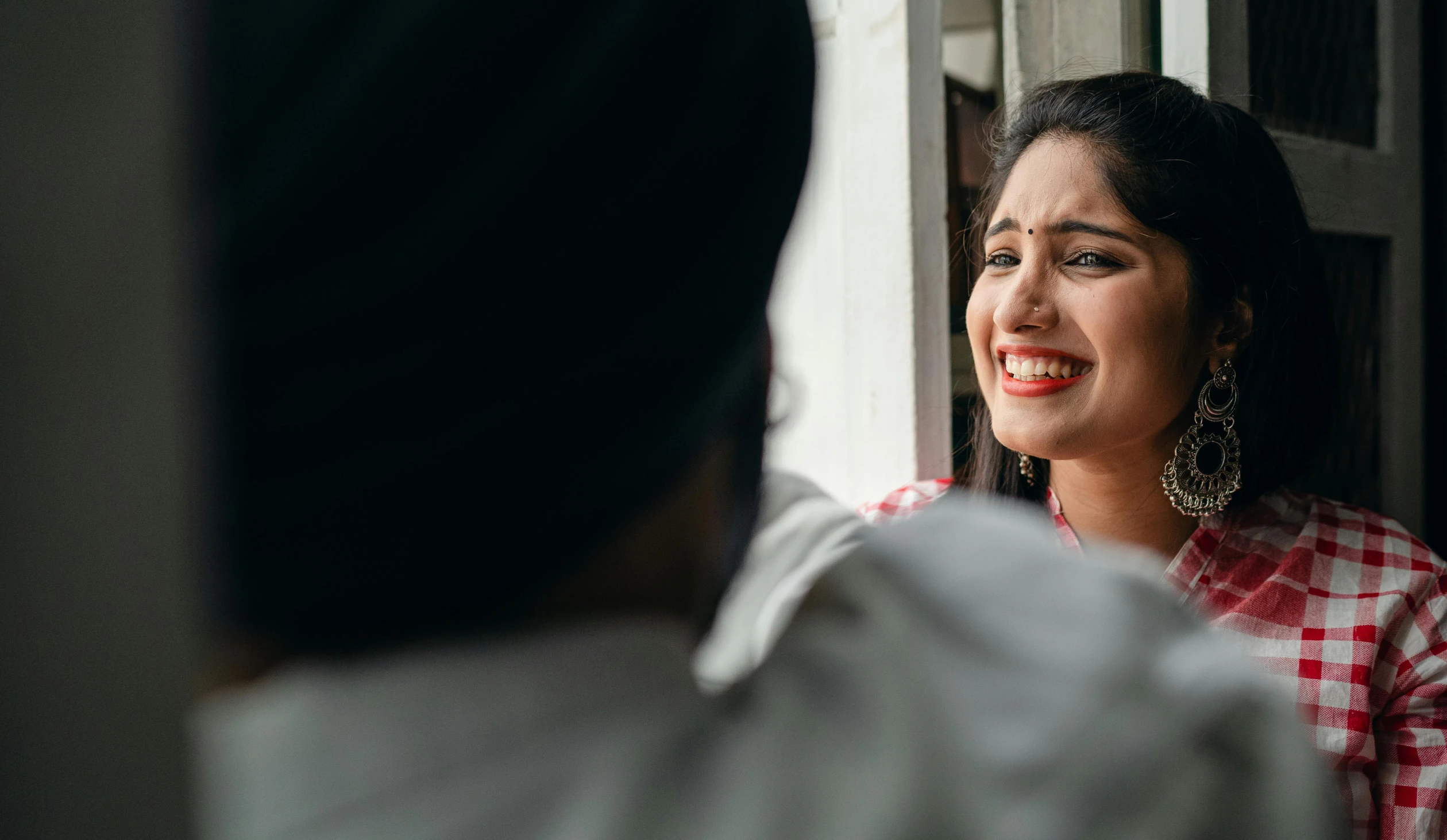 a woman smiles as she looks out a window, pexels contest winner, hurufiyya, smiling couple, frustrated expression, indian, both laughing