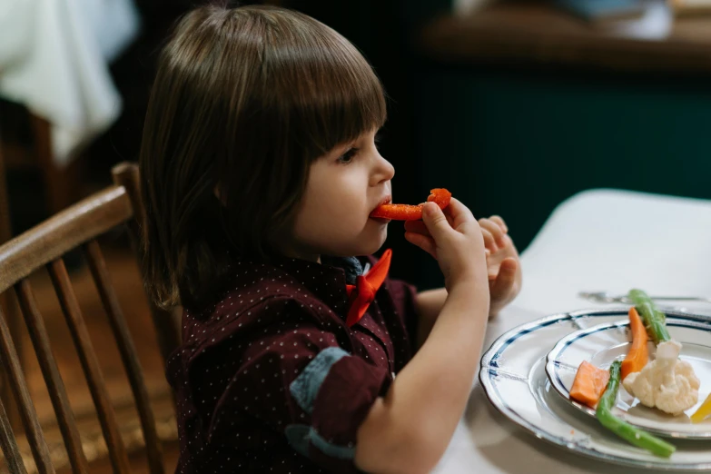 a little girl sitting at a table eating a carrot, by Emma Andijewska, pexels contest winner, dinner is served, profile image, 15081959 21121991 01012000 4k, thumbnail