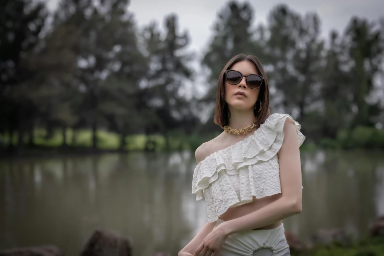 a woman standing in front of a body of water, a picture, inspired by Elsa Bleda, pexels contest winner, renaissance, spiked collar sunglasses, ruffles, at a park, fashion shoot 8k