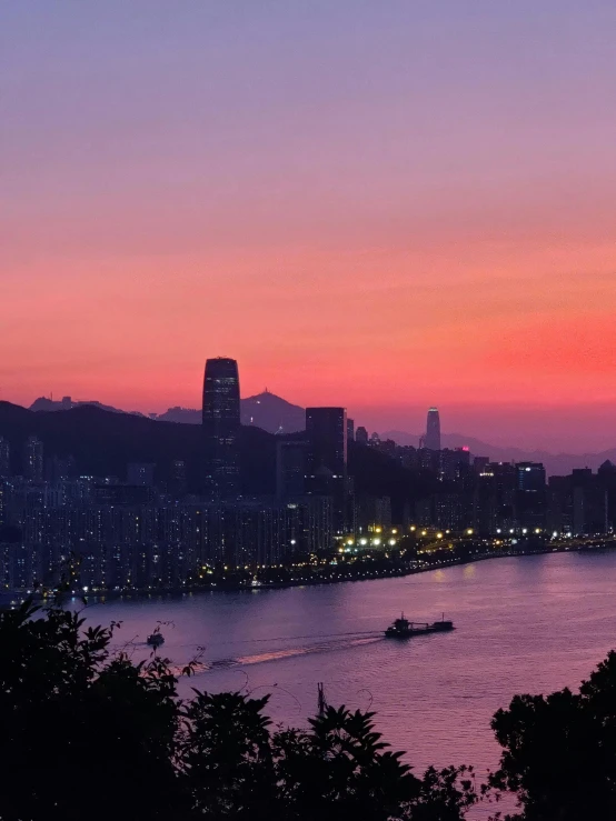 a large body of water with a city in the background, by Patrick Ching, pexels contest winner, happening, pink skies, mountains and ocean, kowloon walled city style, dusk sunset in background