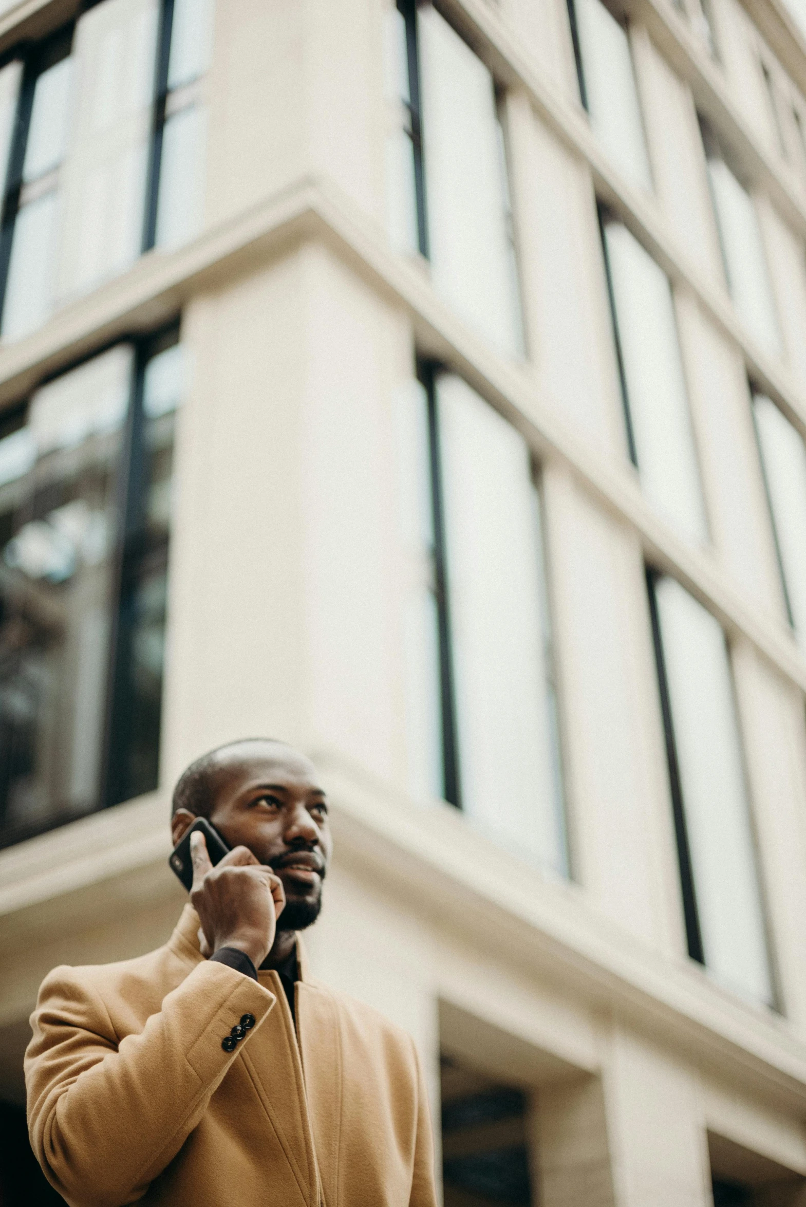 a man standing in front of a tall building talking on a cell phone, black man, top selection on unsplash, brown, coloured