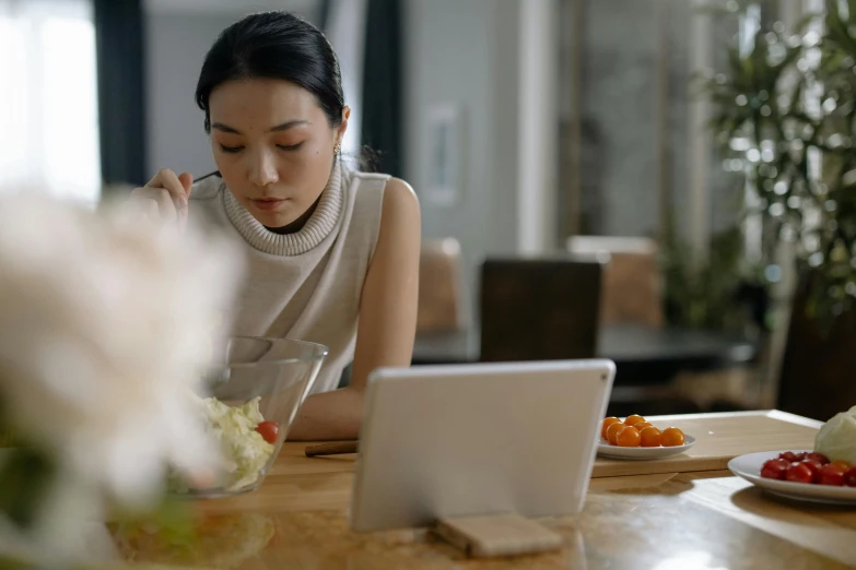 a woman sitting at a table in front of a laptop, inspired by Li Di, trending on pexels, realism, eating, asian descent, using a magical tablet, classy