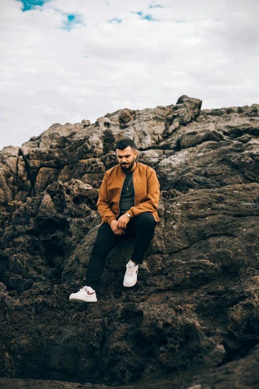 a man sitting on a rock near the ocean, an album cover, trending on unsplash, rugged man portrait, casual pose, charli bowater and artgeem, studio photo