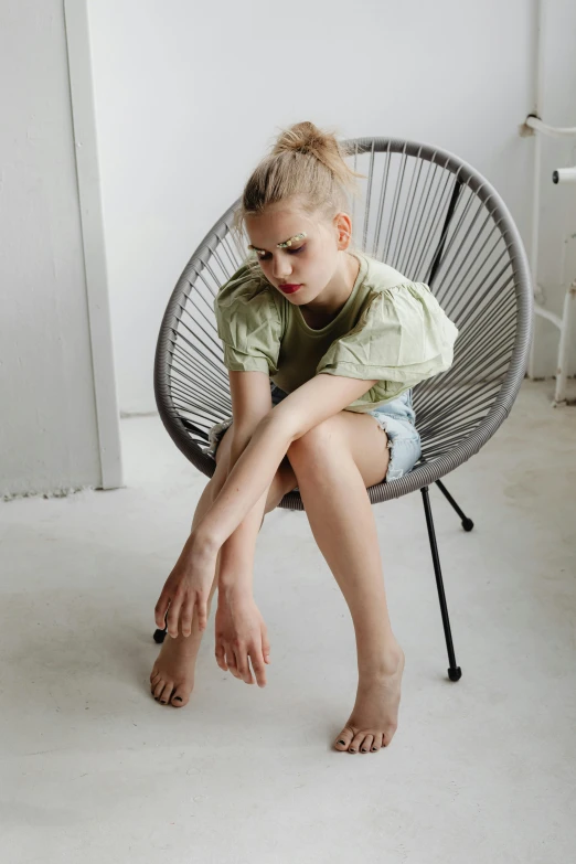 a little girl sitting on top of a chair, by Anna Boch, trending on pexels, olive thigh skin, wearing a light shirt, with depressive feeling, legs intertwined