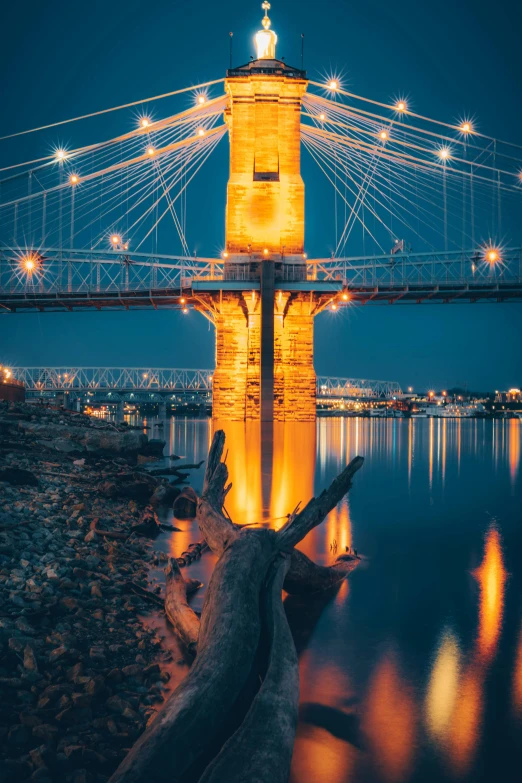 a bridge over a body of water at night, upclose, tn, with orange street lights, tall bridge with city on top