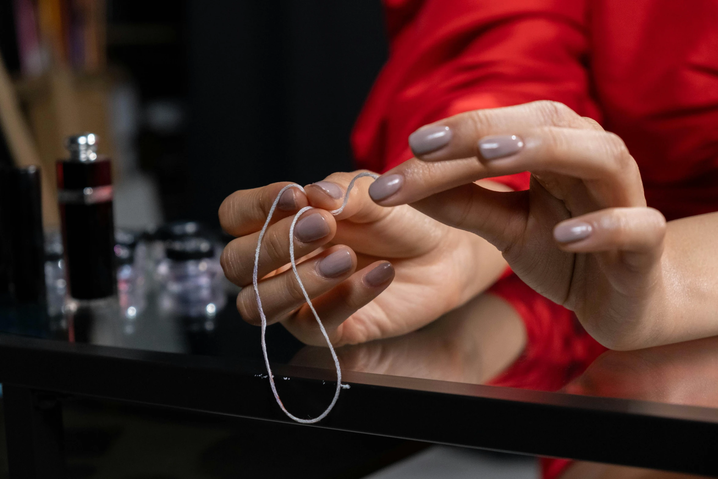 a woman in a red shirt is working on her nails, by Julia Pishtar, pexels contest winner, plasticien, featuring rhodium wires, necklace on display, back of hand on the table, youtube thumbnail
