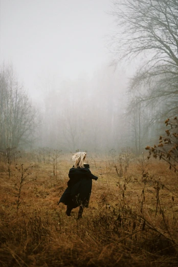 a person standing in a field with trees in the background, inspired by Elsa Bleda, conceptual art, girl with white hair, ominous foggy environment, walking away from camera, andrei tarkovsky
