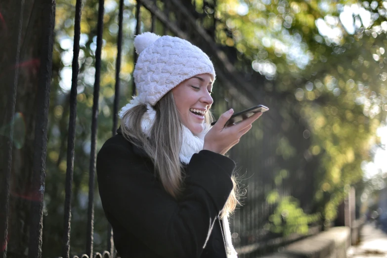 a woman smiles while looking at her cell phone, pexels contest winner, beanie hat, white, autumn season, shouting