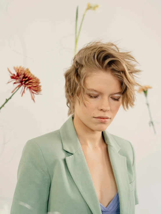 a woman standing in front of a vase of flowers, an album cover, by Ulrika Pasch, trending on unsplash, wearing green suit, wavy short hazel hair, long swept back blond hair, side profile view