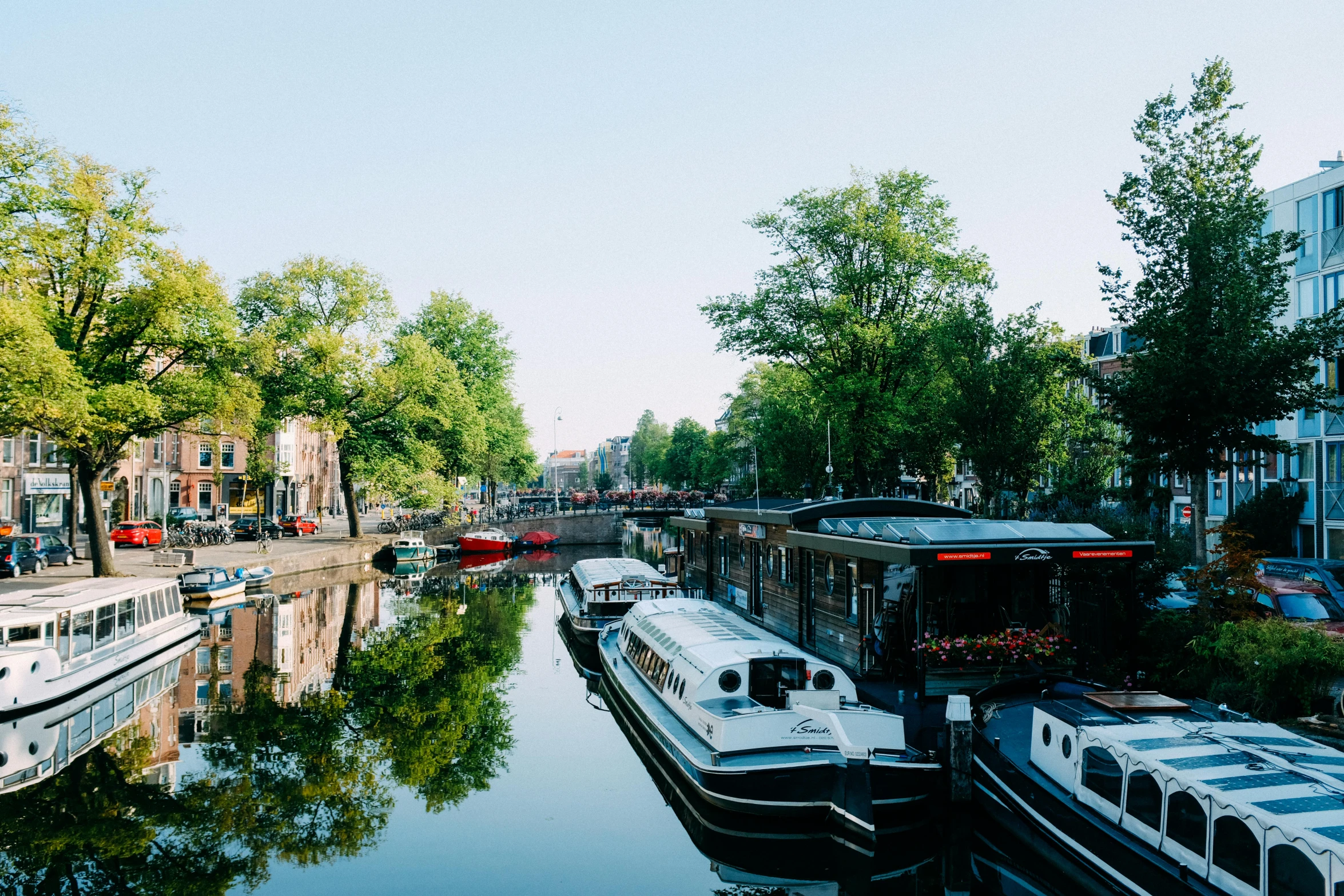 a river filled with lots of boats next to tall buildings, a photo, by Jan Tengnagel, unsplash photography, canal, lush surroundings, van lieven