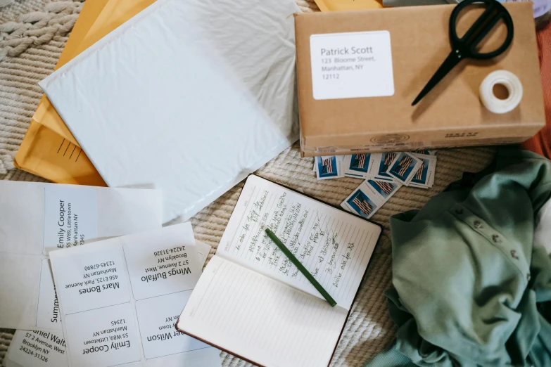 a pile of papers sitting on top of a bed next to a pair of scissors, pexels contest winner, mail art, delivering parsel box, green and brown clothes, writing in journal, wide screenshot