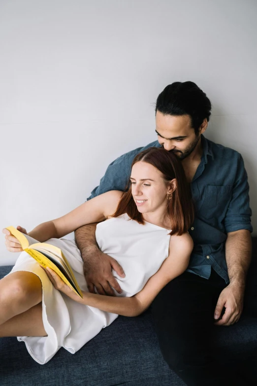 a man and woman sitting on a couch reading a book, pexels contest winner, pregnant belly, looking to his side, bedhead, raphael lecoste