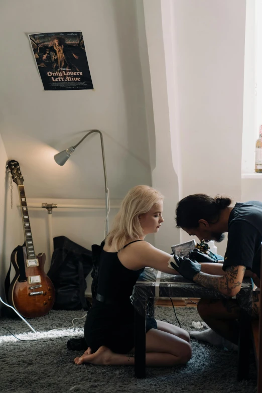 a couple of people that are sitting on the floor, a tattoo, playing a guitar, repairing the other one, kirsi salonen, studio lightning