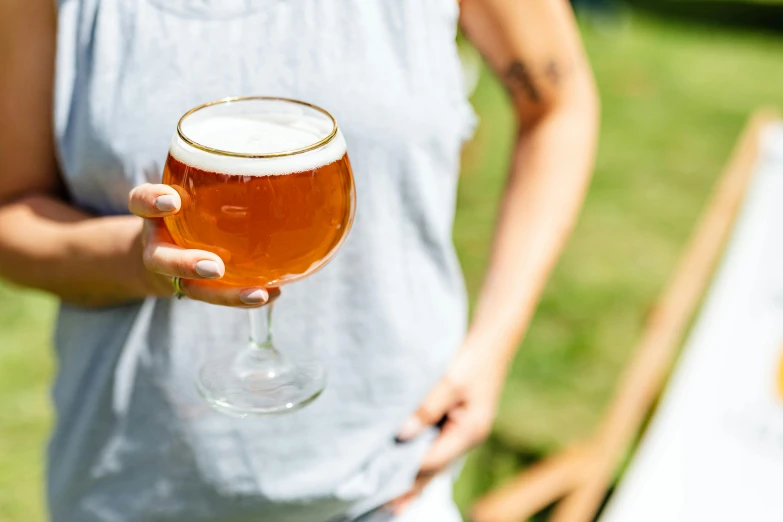 a woman holding a glass of beer in her hand, by Tuvia Beeri, unsplash, private press, garden behind the glasses, round-cropped, new england ipa, glassware