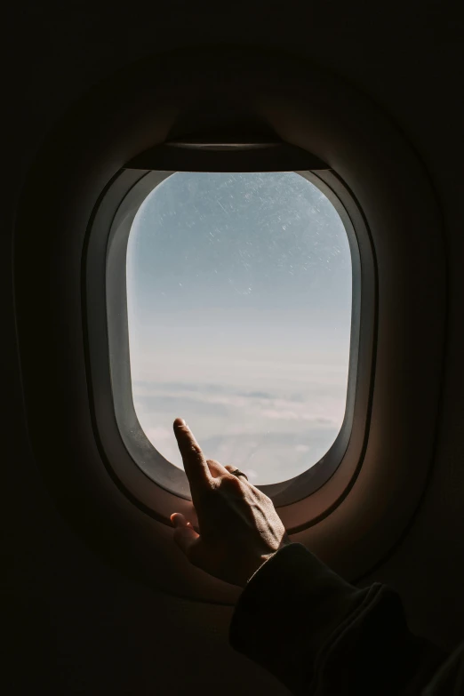 a person looking out an airplane window at the sky, an album cover, pexels contest winner, giving the middle finger, 🚿🗝📝, trending on vsco, in suitcase