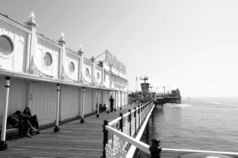 a black and white photo of people sitting on a pier, a black and white photo, pexels, seaside victorian building, arcade, on a bright day, rides