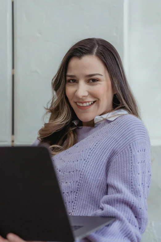 a woman sitting on a couch using a laptop computer, a colorized photo, trending on pexels, purple outfit, wearing sweater, lovely smile, portrait of morana