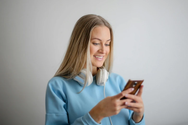 a woman wearing headphones looking at her cell phone, by Adam Marczyński, trending on pexels, happening, wearing a light blue shirt, smiling at camera, wearing casual sweater, avatar image