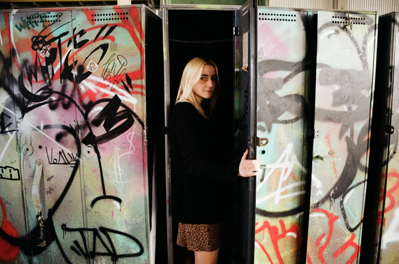 a woman standing in a room with graffiti on the walls, unsplash, graffiti, dakota fanning, lockers, portrait image, exiting from a wardrobe