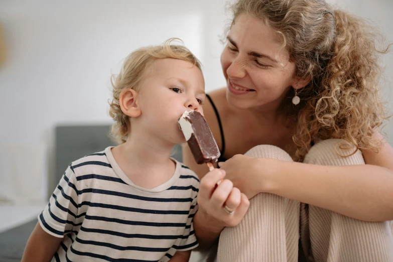 a woman sitting next to a child eating an ice cream bar, pexels contest winner, incoherents, brown and cream color scheme, manuka, at home, profile image