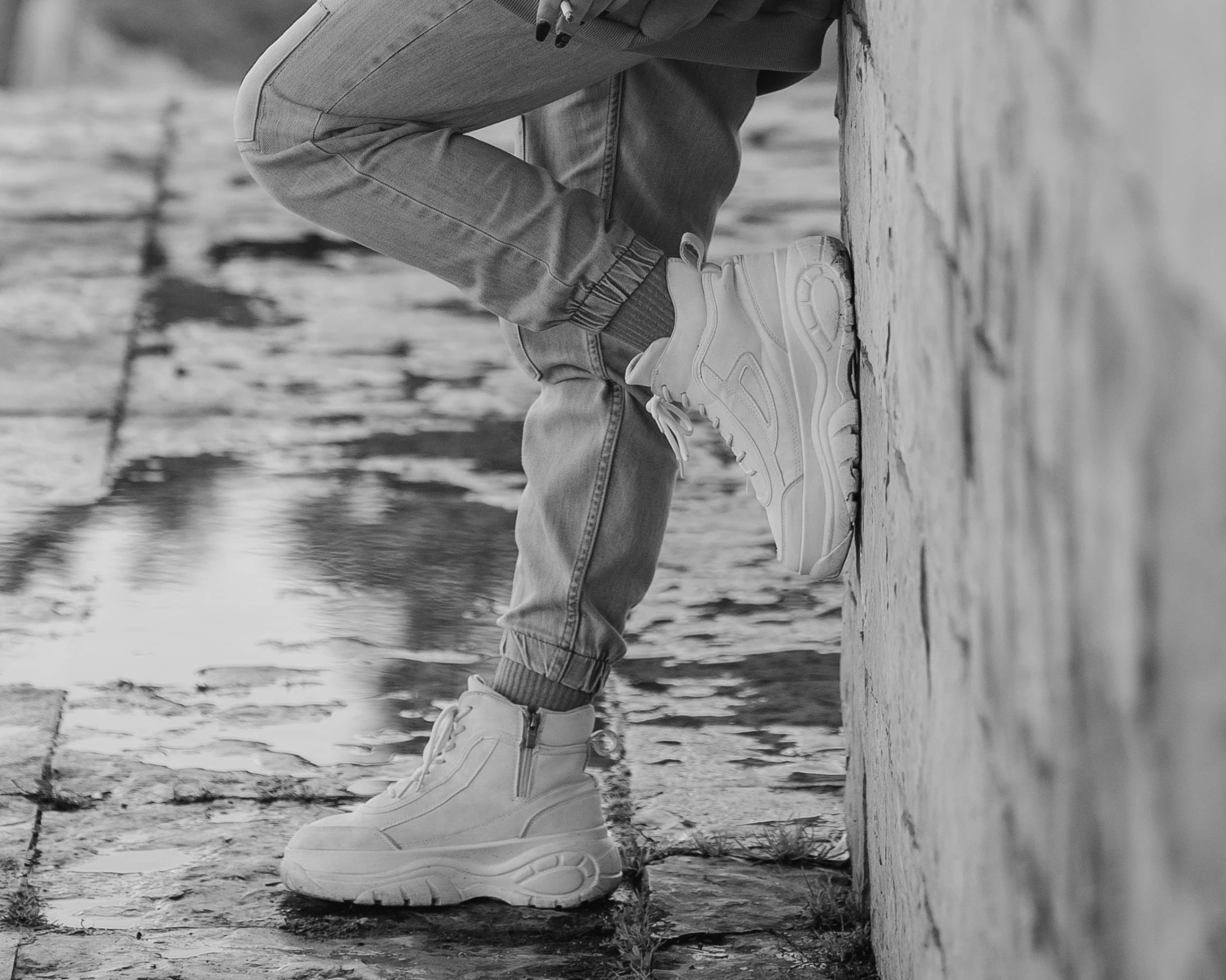 a black and white photo of a man leaning against a wall, an ambient occlusion render, pexels, realism, futuristic balenciaga sneakers, standing in a pond, beige, jeans and boots