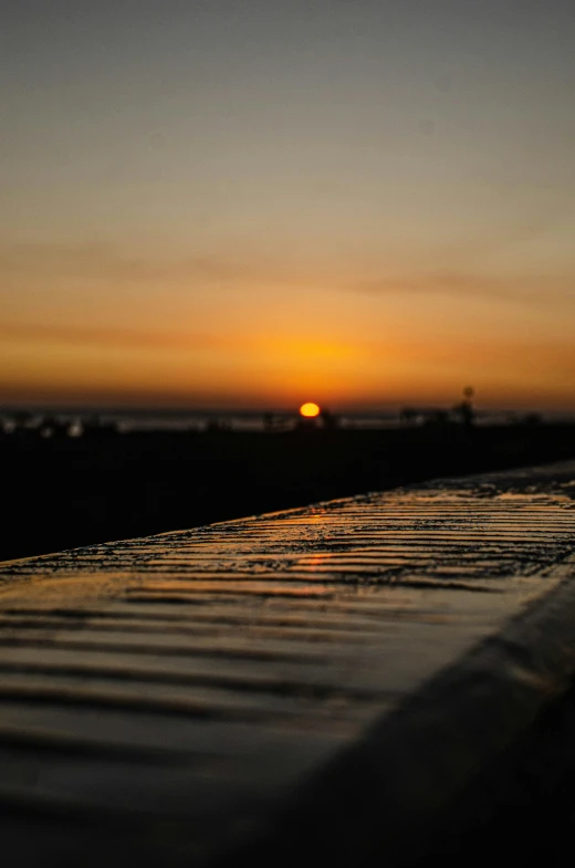 the sun is setting over the water on the beach, a picture, unsplash, happening, bench, wet surface, full frame image, upclose